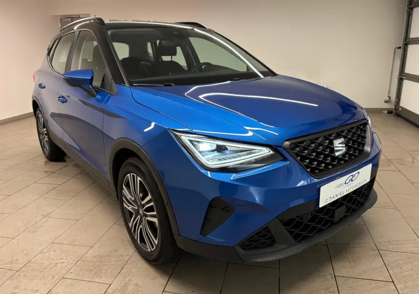Vue 3/4 avant droite du SEAT Arona 2025 en bleu saphir avec toit noir, mettant en valeur sa calandre et ses phares LED.