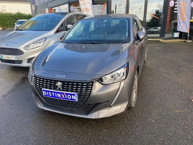 Peugeot 208 gris platinium vue 3/4 avant droit, avec calandre distinctive et phares LED allumés.