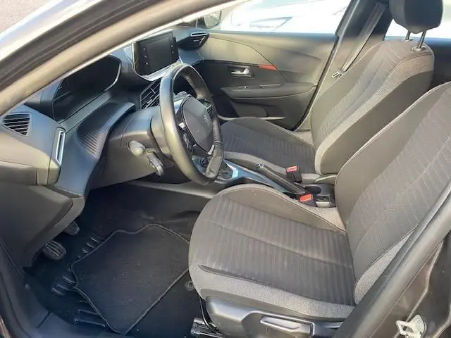 Vue intérieure côté conducteur de la Peugeot 208 gris platinium, sièges tissu noir et tableau de bord moderne avec écran tactile.