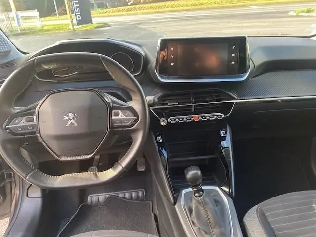 Vue intérieure de face du poste de conduite gris noir de la Peugeot 208 2021 avec volant compact et écran tactile central.