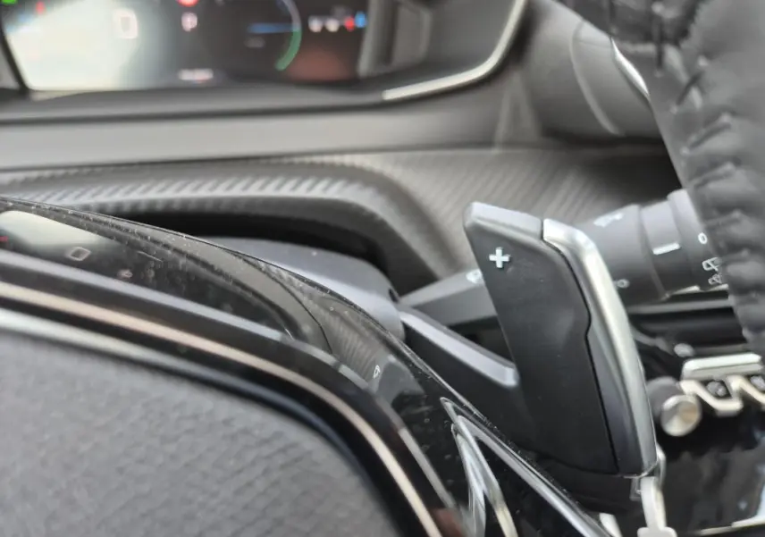 Gros plan sur la palette de changement de vitesse droite du volant dans l’habitacle noir du Peugeot 208 Hybrid 110 e-DCS6 Allure.