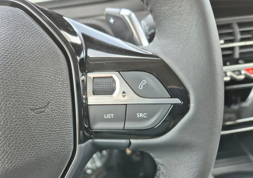Gros plan sur les commandes gauche du volant cuir d’une Peugeot 208 blanche, avec boutons de téléphone et réglages audio.