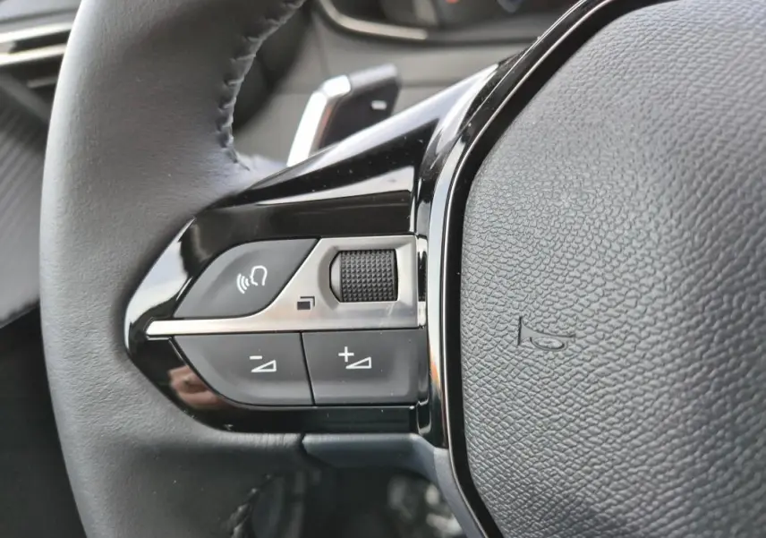 Gros plan sur la partie gauche du volant de la Peugeot 208 Hybrid 110 e-DCS6 Allure 2025, avec commandes audio intégrées.