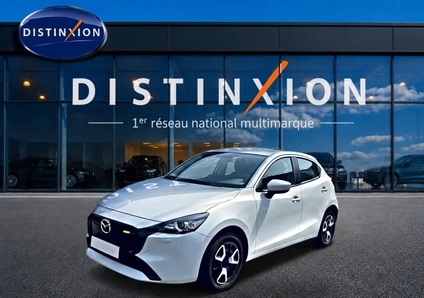 Vue 3/4 avant droite d'une Mazda2 blanche 2024 avec jantes noires et calandre noire devant un showroom Distinxion.