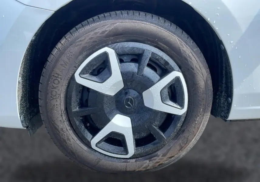 Gros plan sur la roue avant droite d’une Mazda2 blanche avec enjoliveur noir et argenté au design triangulaire.