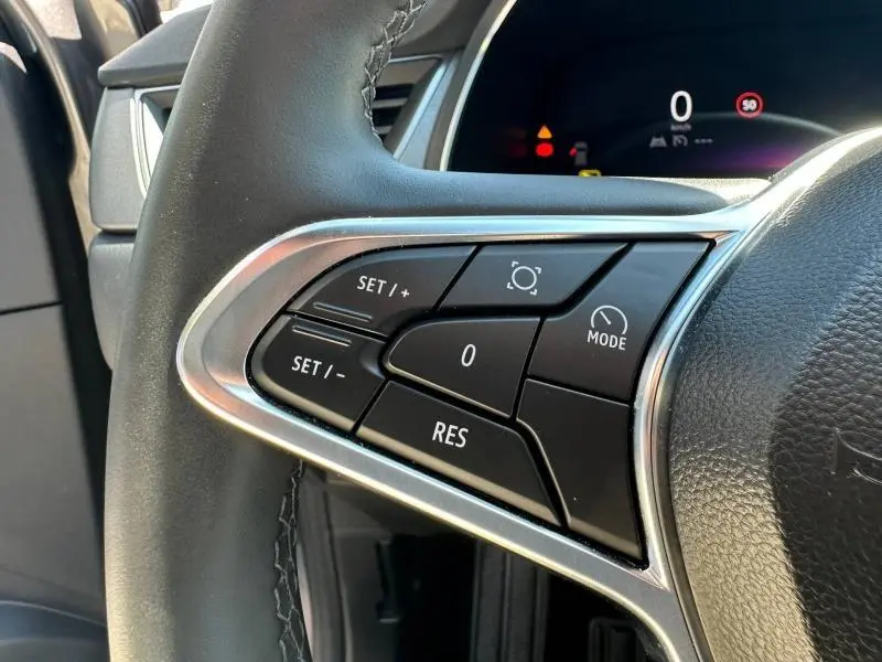 Gros plan sur les commandes au volant du Renault Captur gris Cassiopée, avec affichage numérique en arrière-plan.