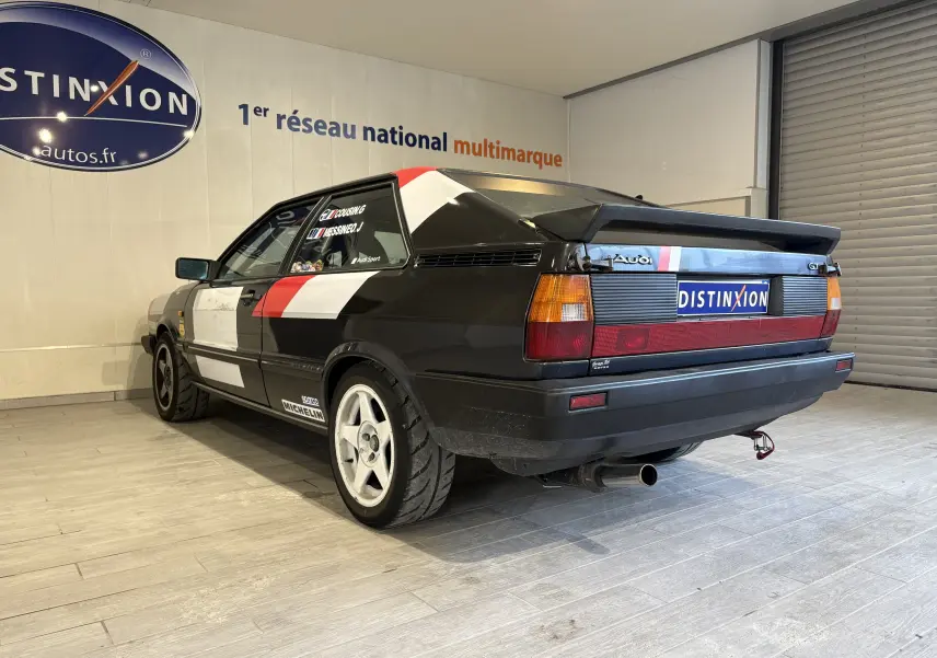 Gros plan intérieur sur les sièges baquets noirs GT2i avec harnais rouges dans un Audi Coupé GT noir de 1983 équipé pour rallye.