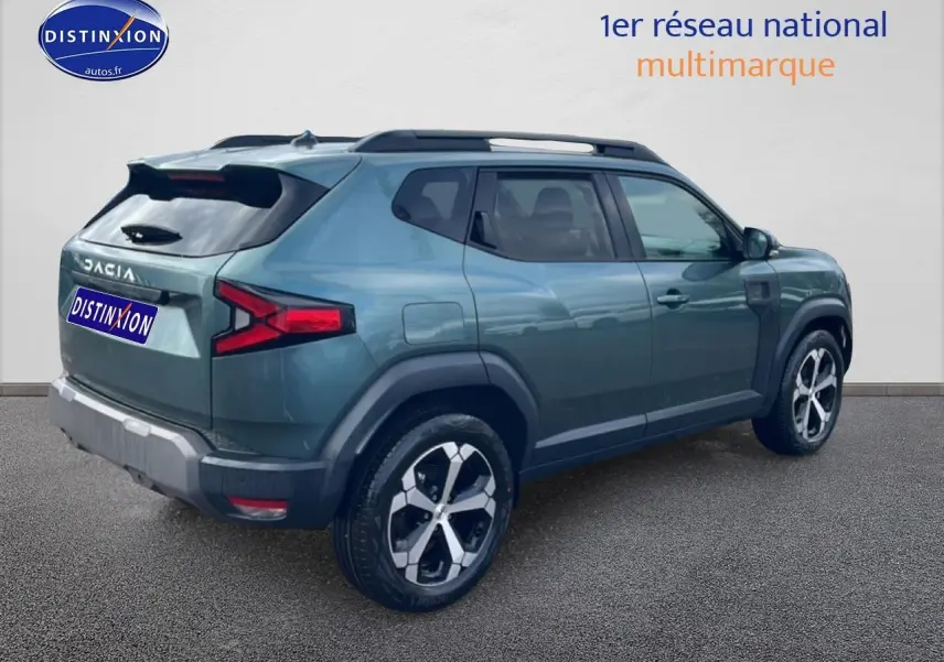 Vue 3/4 arrière droite du Dacia Duster 2026 vert cèdre avec jantes alu et barres de toit visibles.