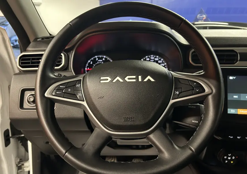 Vue rapprochée du volant noir du Dacia Duster 2025, avec commandes intégrées et tableau de bord en arrière-plan.