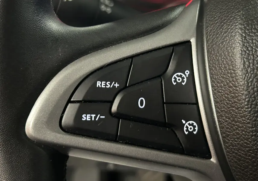 Gros plan sur les commandes de régulateur de vitesse au volant noir du Dacia Duster blanc 2025.