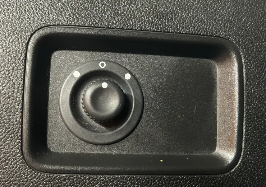 Gros plan sur le bouton de réglage des rétroviseurs noirs dans l'habitacle du Dacia Duster blanc 2025.