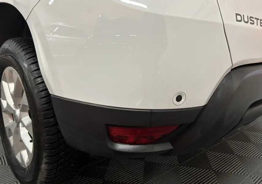 Gros plan sur l'arrière droit blanc du Dacia Duster 2025, avec feu rouge et capteur de stationnement visible.