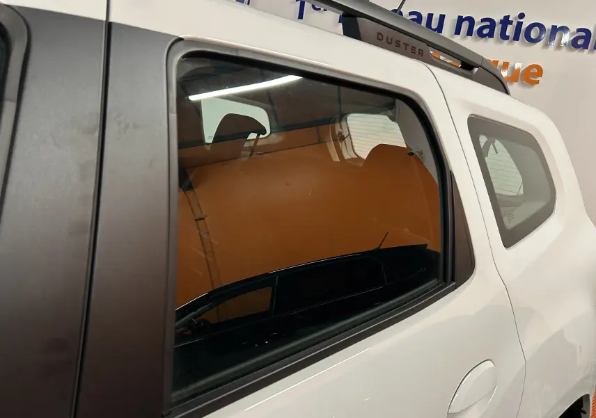 Vue latérale droite sur la partie arrière d'un Dacia Duster blanc 2025 avec toit noir et barres de toit Duster visibles.