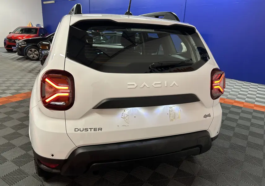 Vue arrière d'un Dacia Duster blanc 2025 avec feux arrière allumés dans un showroom.