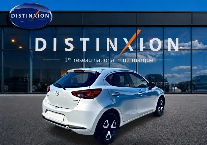 Vue 3/4 arrière droite d'une Mazda2 blanche 2024 stationnée devant une vitrine Distinxion.