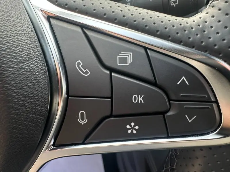 Gros plan sur les commandes noires au volant cuir perforé du Renault Symbioz rouge flamme, boutons multifonctions visibles.