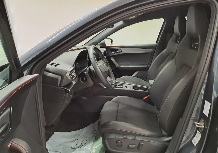 Vue intérieure côté conducteur de la CUPRA Leon 2023 avec sièges sport noirs et surpiqûres orange, tableau de bord moderne.