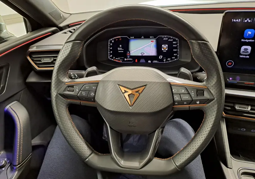 Vue intérieure centrée sur le volant perforé de la CUPRA Leon 1.5 TSI 150 DS7 V avec logo cuivré et tableau de bord numérique.