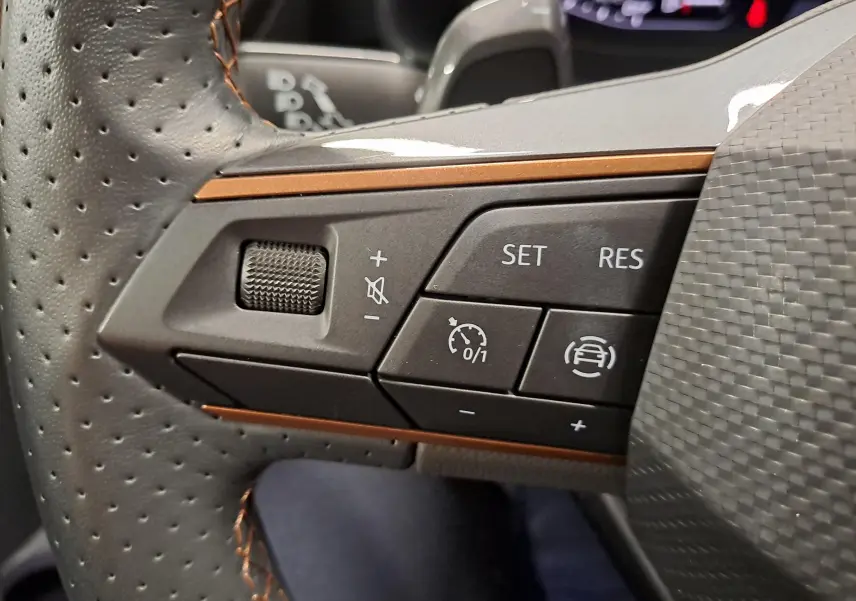 Gros plan sur les commandes à gauche du volant perforé avec surpiqûres cuivrées de la CUPRA Leon gris magnétique 2023.