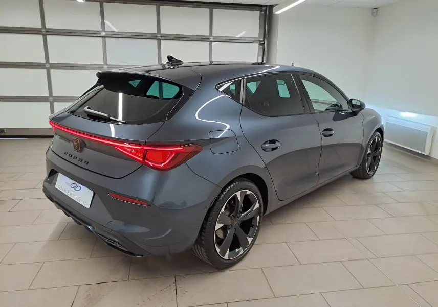 Vue 3/4 arrière droite d'une CUPRA Leon 2023 gris magnétique avec feux arrière allumés et jantes noires distinctives.