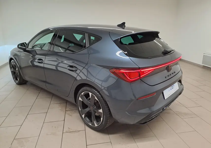 Vue 3/4 arrière droite d'une CUPRA Leon 2023 gris magnétique avec feux arrière allumés et jantes noires distinctives.