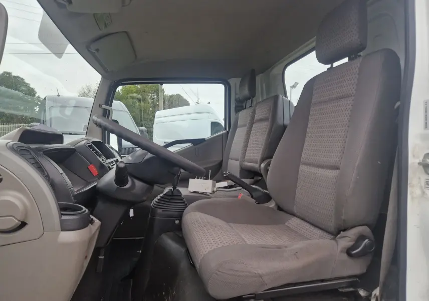 Vue intérieure côté conducteur du Nissan Cabstar blanc 2010, montrant les sièges et le volant avec boîte manuelle.