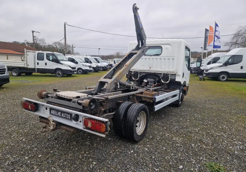 Vue 3/4 arrière droite du Nissan Cabstar blanc 2010 avec châssis cabine et bras polybenne visible.