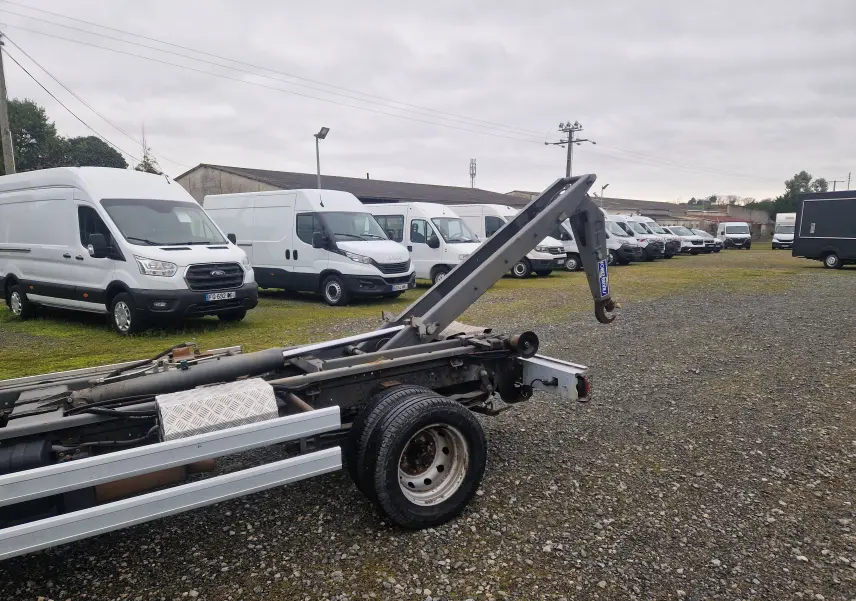 Vue arrière côté droit du châssis cabine blanc Nissan Cabstar 2010 avec bras polybenne déployé sur un terrain gravillonné.