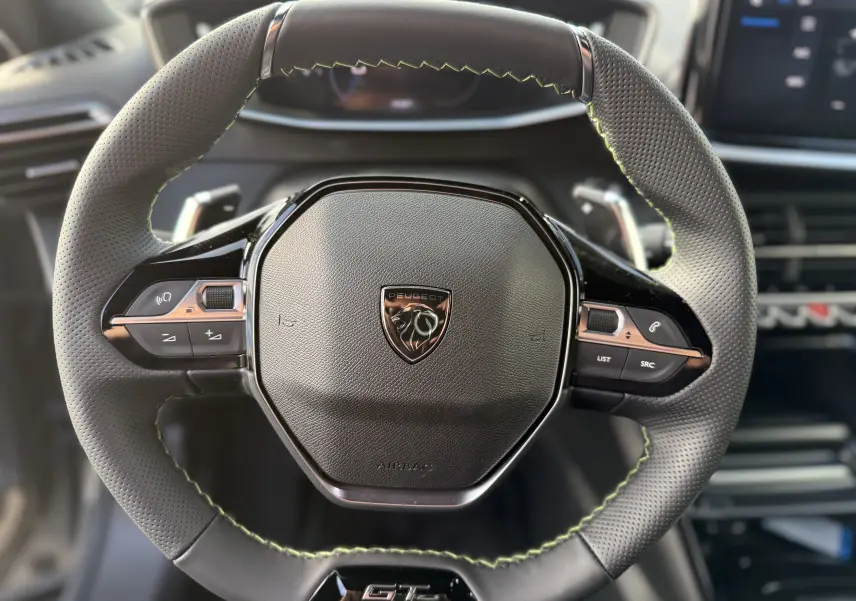 Vue rapprochée du volant cuir perforé avec coutures vertes et logo Peugeot du SUV 2008 Hybrid 145ch GT 2025.