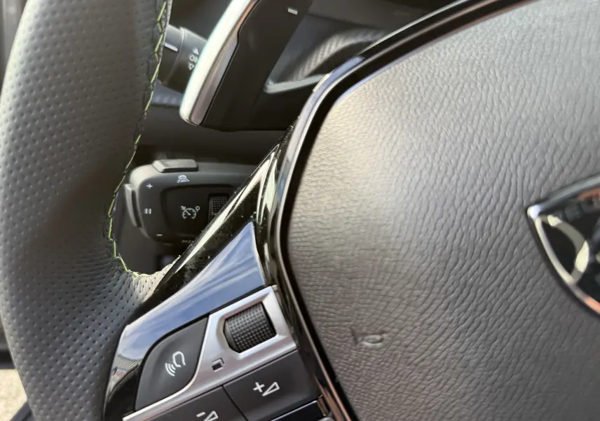 Gros plan sur le volant en cuir perforé du Peugeot 2008 Hybrid 145ch GT, mettant en valeur les commandes intégrées.