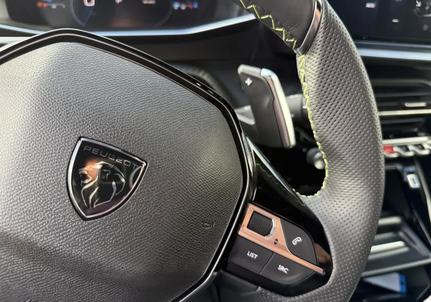 Gros plan sur le volant perforé du Peugeot 2008 Hybrid 145ch GT 2025 avec logo lion et commandes intégrées.