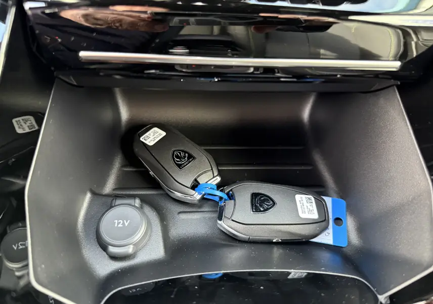 Gros plan intérieur sur la console centrale d’une Peugeot 2008 gris selenium, avec deux clés hybrides posées à côté d’une prise 12V.