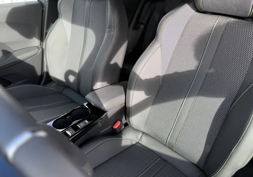 Gros plan sur les sièges avant gris avec surpiqûres vertes du Peugeot 2008 Hybrid 145ch GT 2025, intérieur moderne et soigné.