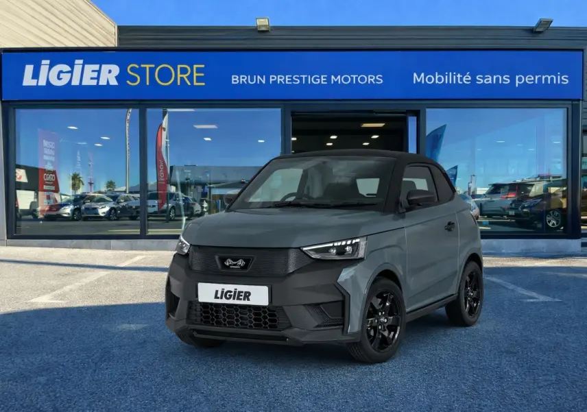 Vue 3/4 avant d'une Ligier JS50 Elite Revo D+ gris graphite avec toit noir, stationnée devant un showroom Ligier.