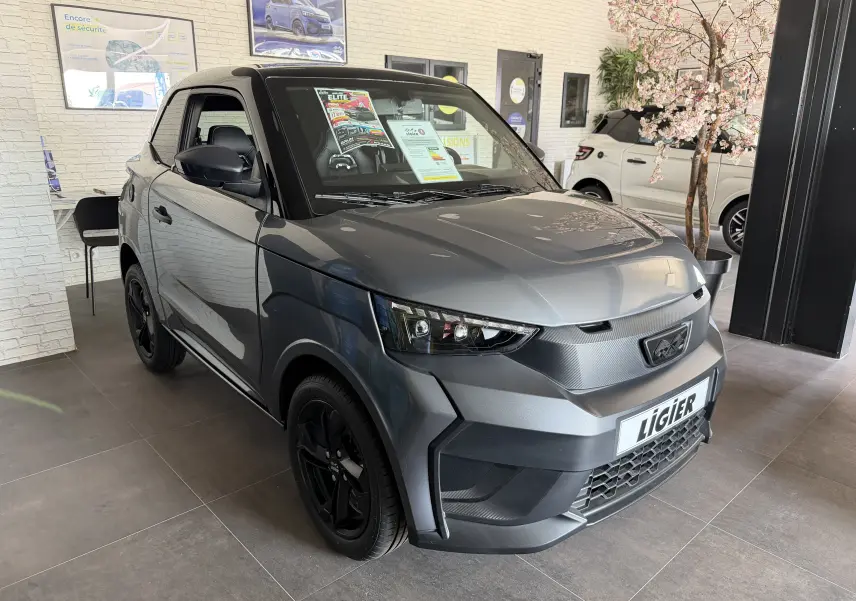 Vue 3/4 avant d'une Ligier JS50 Elite Revo D+ gris graphite avec jantes noires, exposée en showroom lumineux.