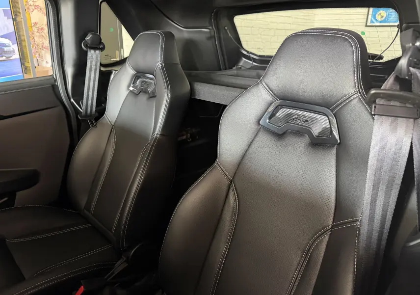 Vue intérieure rapprochée des sièges avant en cuir noir avec surpiqûres blanches du Ligier JS50 Elite Revo D+ gris graphite.