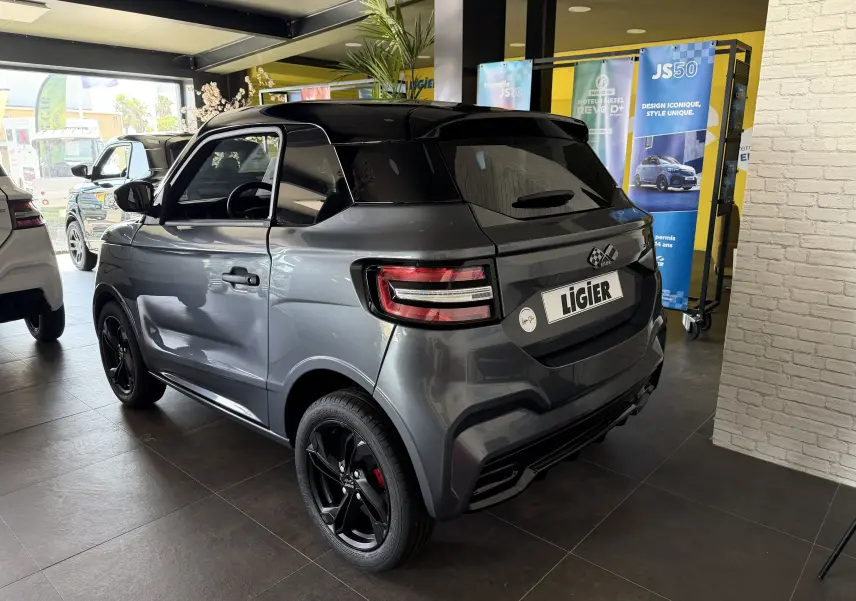 Vue 3/4 arrière droite d'une Ligier JS50 Elite Revo D+ gris graphite avec toit noir et jantes noires en showroom.