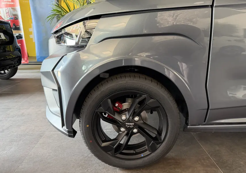 Gros plan sur la roue avant gauche noire et la carrosserie gris graphite d'une Ligier JS50 Elite Revo D+ en concession.