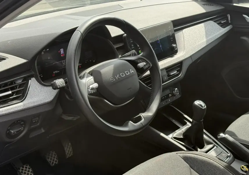 Vue intérieure côté conducteur du Skoda Scala TSI 116 gris graphite, volant cuir et levier de vitesses manuel visibles.
