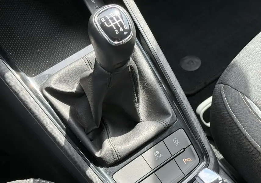 Gros plan sur le levier de vitesses manuel noir de la Skoda Scala TSI 116, entouré de boutons de contrôle sur console centrale.