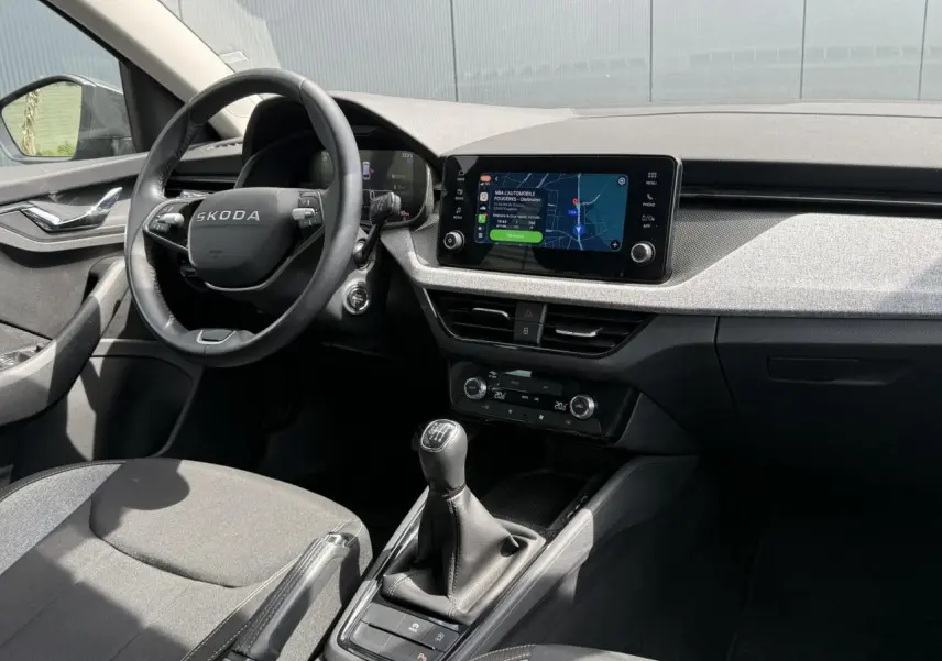 Vue intérieure côté conducteur de la Skoda Scala TSI 116 gris graphite, volant cuir et écran tactile central allumé.