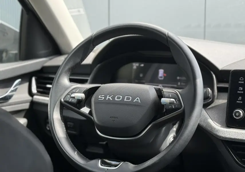 Vue rapprochée du volant en cuir noir avec logo SKODA au centre, tableau de bord et écran tactile visibles en arrière-plan.