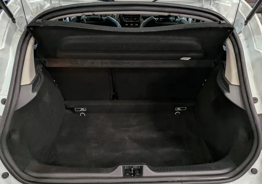 Coffre ouvert vu de l'arrière d'une Renault Clio IV blanc glacier, montrant l'espace de chargement vide et la plage arrière relevée.