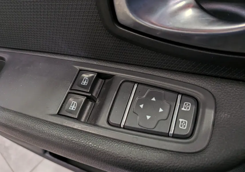 Gros plan sur les commandes de lève-vitres et réglage des rétroviseurs côté conducteur d'une Renault Clio IV blanche.