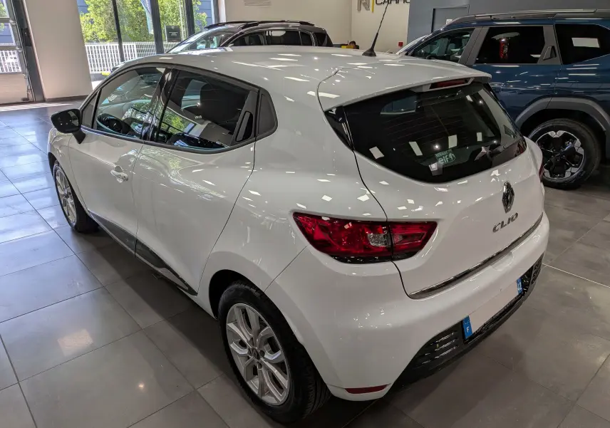 Renault Clio IV blanc glacier vue 3/4 arrière droit en intérieur, avec feux arrière rouges et jantes alliage.