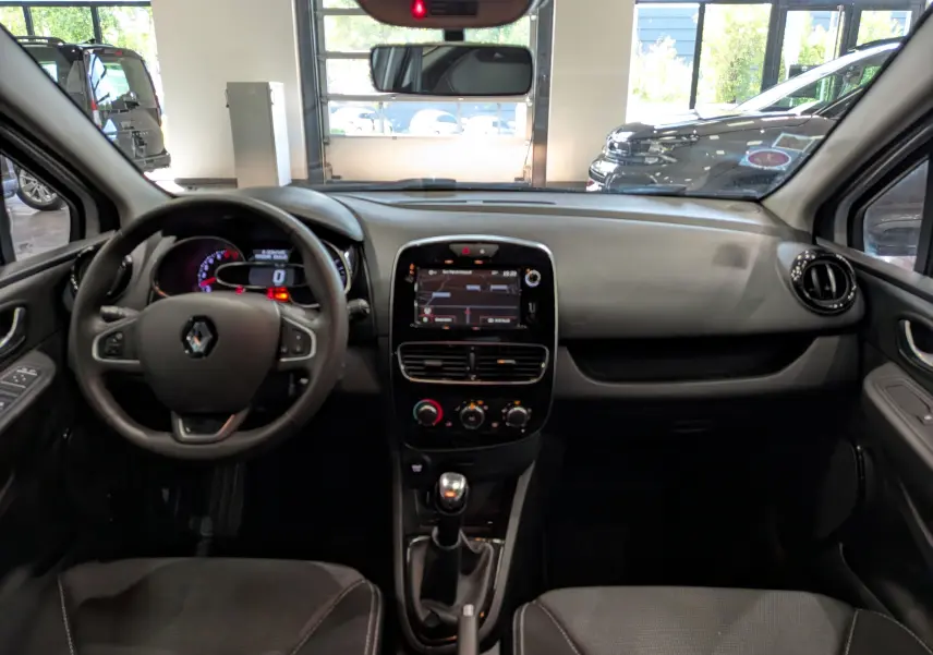 Vue intérieure frontale du tableau de bord et volant de la Renault Clio IV TCe 75 blanche avec écran tactile et boîte manuelle.
