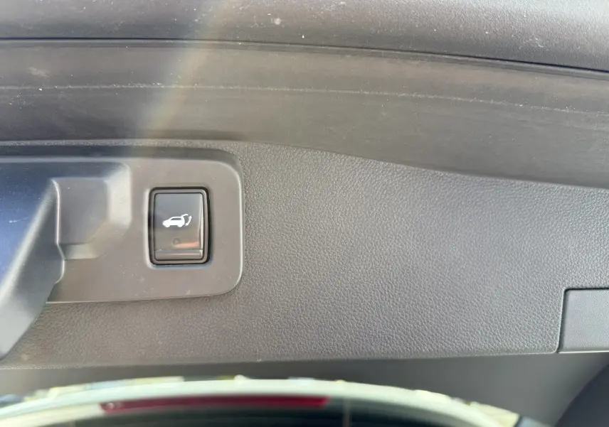 Gros plan sur le bouton d'ouverture électrique du coffre, intégré dans le panneau intérieur noir du hayon du Renault Austral blanc.
