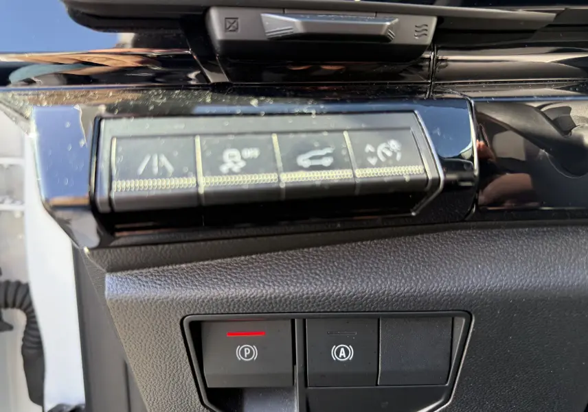 Gros plan sur les commandes intérieures du tableau de bord du Renault Austral blanc, avec boutons d'assistance et frein à main électronique.