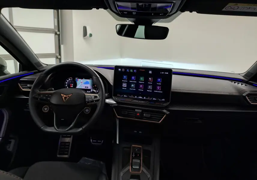Vue intérieure du tableau de bord de la CUPRA LEON ST 2025 avec écran tactile central et éclairage d’ambiance bleu.