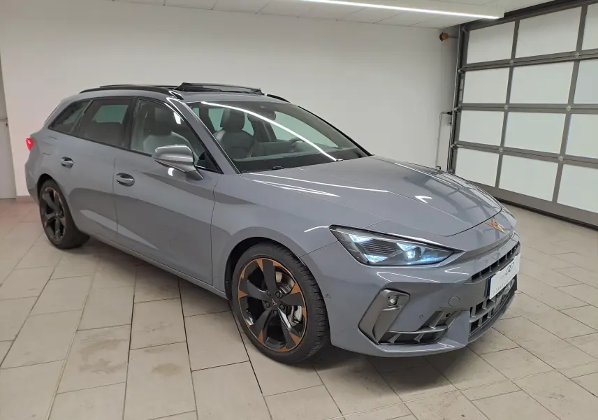 Vue 3/4 avant d’une CUPRA Leon ST gris Graphène avec jantes cuivrées et toit ouvrant panoramique en intérieur.